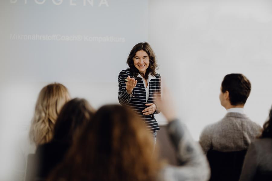 Person zeigt während einem Vortrag der Biogena Academy auf - Referentin bittet die Frage zu stellen.