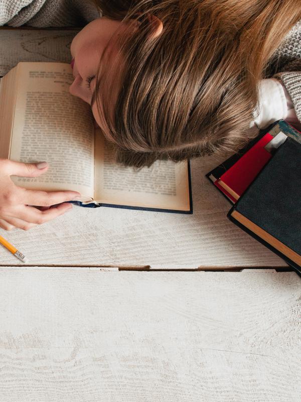 Frau müde und erschöpft schläft auf dem Schreibtisch während des Lernens ein