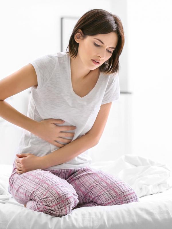 Frau sitzt mit krampfendem Bauch auf dem Bett und hält sich schmerzverzerrt den Magen und Darm