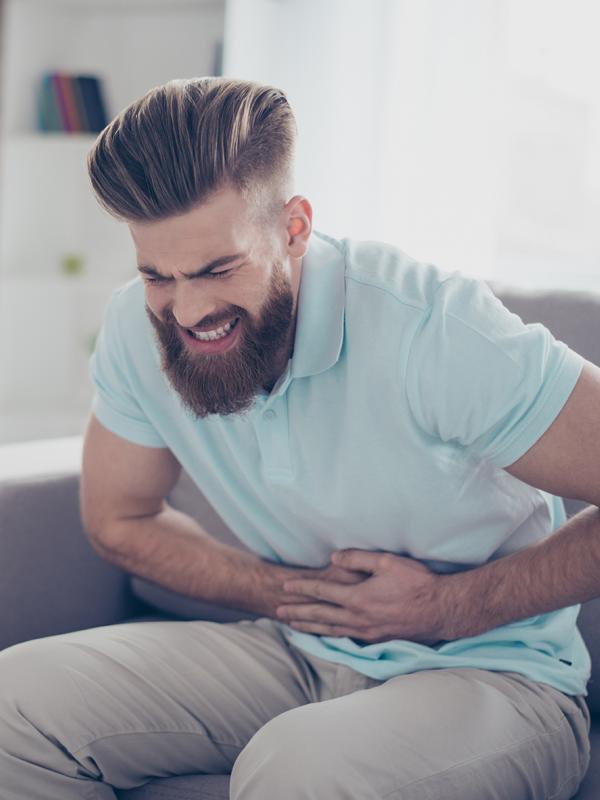 Mann hält sich schmerzverzerrt den Bauch und drückt sich auf Magen und Darm