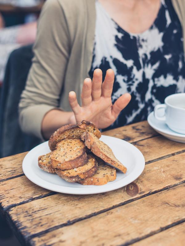 Frau schiebt Teller mit Brot weg