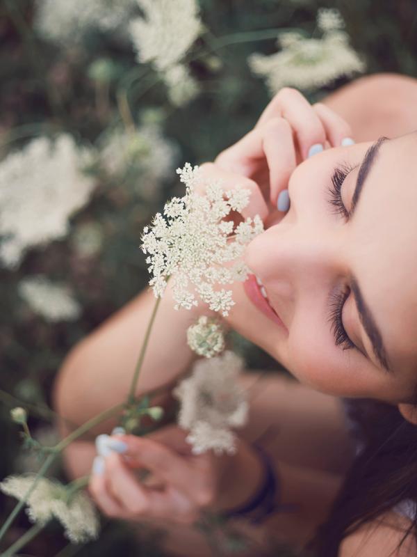 Frau sitzt in einer Wiese, riecht an einer Blume und genießt das Leben