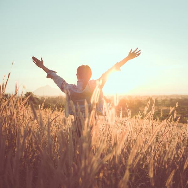 Frau steht bei Sonnenschein fröhlich und voller Energie auf einem Feld 