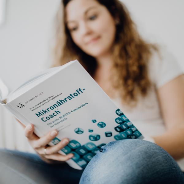Frau sitzt auf Sofa, hat das MikronährstoffCoach Buch aufgeschlagen und blättert interessiert darin
